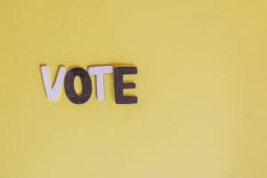 Pink and purple letters spelling "VOTE" against a yellow background
